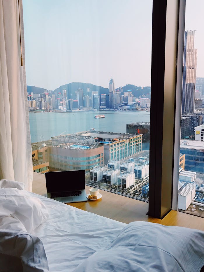 Cozy hotel room with cityscape view from bed, featuring a laptop and coffee by the window.
